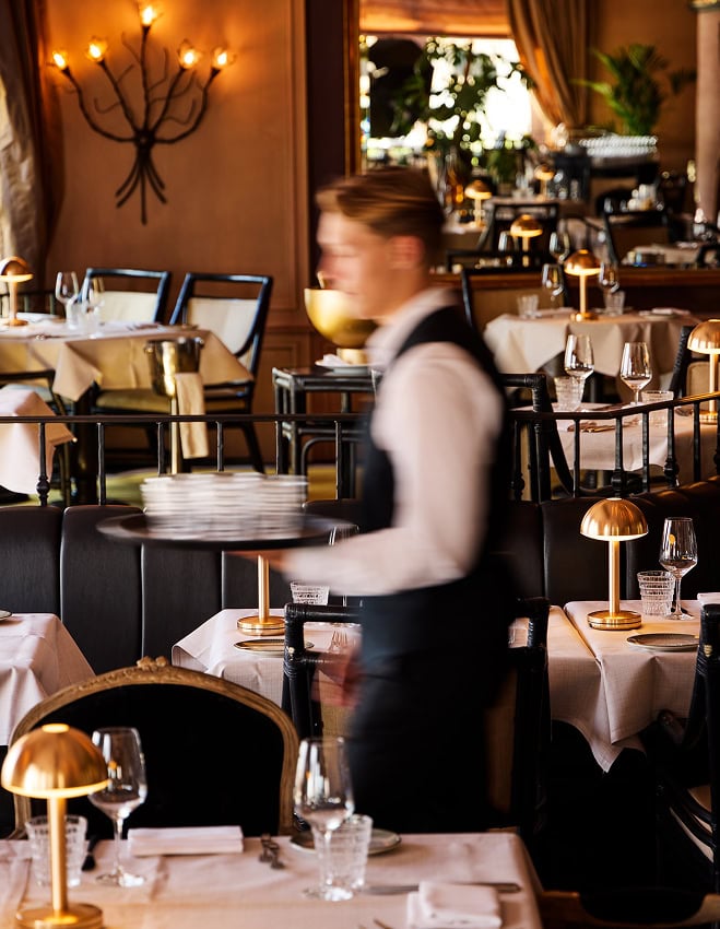 Ober schenkt wijn in bij een gedekte tafel in het restaurant